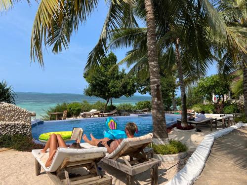 2 personnes assises sur des chaises longues près d'une piscine dans l'établissement Z-Lodge Zanzibar, à Kiwengwa