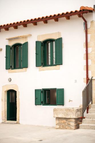 a white building with green shuttered windows at Traditional Anna's Stone House with Private Pool in Margarítai