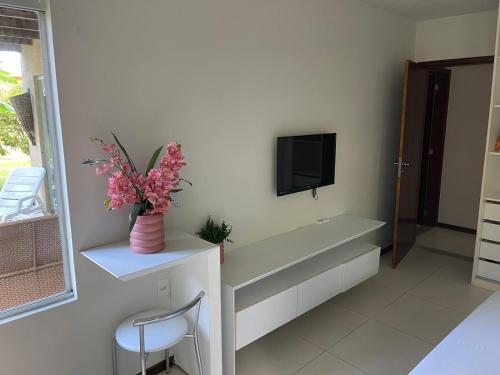 a white room with a tv and a vase with flowers at Apartamento Villas do Pratagy in Maceió