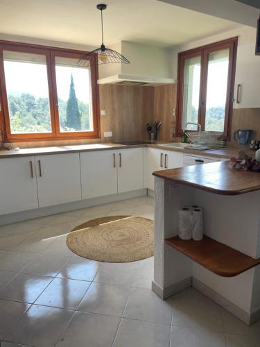 une cuisine avec des placards blancs, une table et des fenêtres dans l'établissement Charme provençal près de Nice, à Blausasc