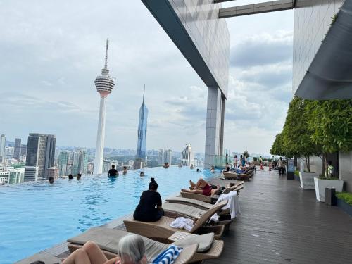 a infinity pool on the top of a building with people sitting on chairs at The Platinum KLCC By Staycation in Kuala Lumpur