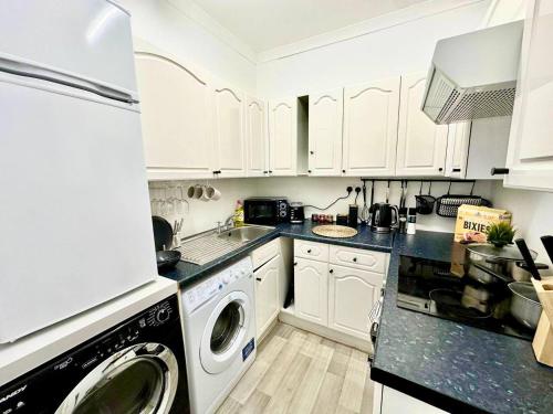 a kitchen with white cabinets and a washer and dryer at Cosy stylish Dumbarton flat in Dumbarton