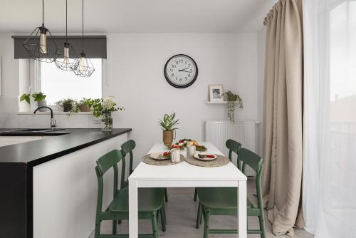 a kitchen with a table with green chairs and a clock at TS Hello City Apartment in Szczecin