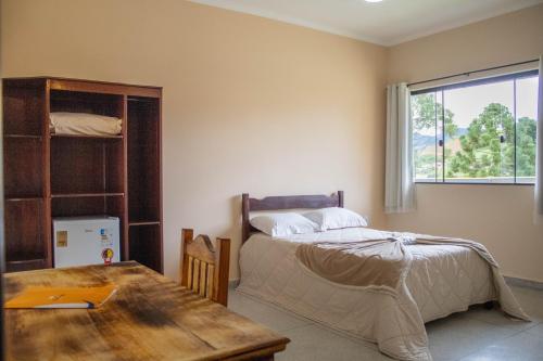 a bedroom with a bed and a table and a window at Hotel Águas Lindas in Itamonte