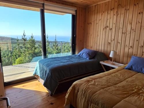 two beds in a room with a large window at Casa Bosquemar Boyeruca in Vichuquén