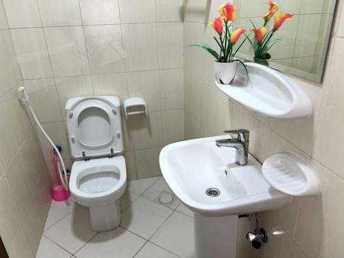 a bathroom with a sink and a toilet with flowers at Small Room shared bath with beach access for single person or short stay couplesغرفة صغيرة مع حمام مشترك مع إمكانية الوصول إلى الشاطئ لشخص واحد أو للأزواج الذين يقيمون لفترة قصيرة in Ajman