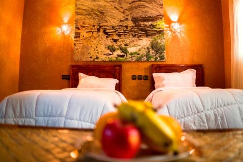 two beds in a room with a plate of fruit on a table at Riad ait Ben Haddou in Aït Ben Haddou