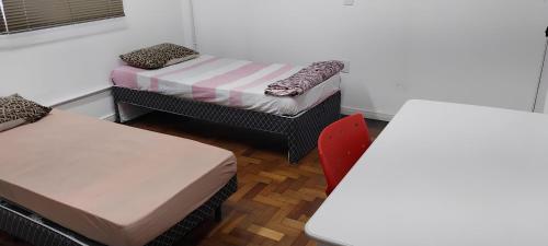 a room with two beds and a table and a chair at Aloha Hostel&CoWorking - Prox Aeroporto e Consulado in Porto Alegre