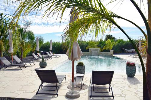 uma piscina com cadeiras e um guarda-sol e uma mesa e cadeiras em Antico Casale Benalì em Siracusa