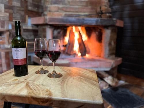 two glasses of wine on a table with a fireplace at Cabaña en la Calera BersaNina in La Calera
