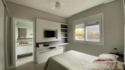 ein Schlafzimmer mit einem Bett und einem Waschbecken sowie einem TV in der Unterkunft Condomínio de Alto Padrão a 250m da Praia in Xangri-lá