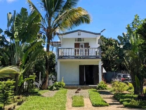a white house with a balcony and palm trees at Chez GG in Toamasina