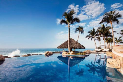 uma piscina num resort com palmeiras e o oceano em One&Only Palmilla em San José del Cabo