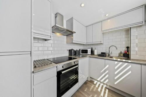 Stylish 2 bedroom Apartment in Kettering Town Centre, sleeps 4, free parking, wifi, Sky, Netflix في نورثامبتون: مطبخ أبيض مع دواليب بيضاء ومغسلة
