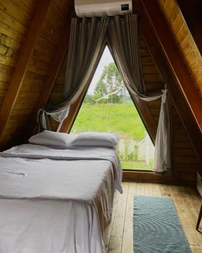 uma cama num quarto com uma grande janela em Refúgio prox Ctba Chalé Suíço 50m2, 400 m2 de área em Mandirituba