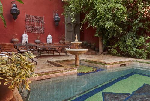 une fontaine en face d'un bâtiment rouge avec une piscine dans l'établissement Riad Les Jardins d'Henia, à Marrakech