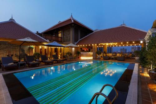 una piscina por la noche con sillas y sombrillas en Jaya Suites Hotel en Phnom Penh