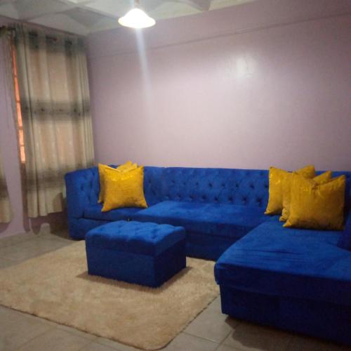 uma sala de estar com um sofá azul e almofadas amarelas em Verona Apartments em Thika