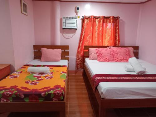 2 camas en una habitación pequeña con paredes rosas en JayDin Travellers Inn en Panglao