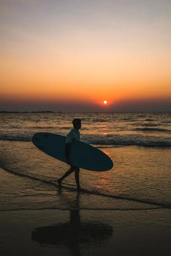 a man walking on the beach with a surfboard at Blue Lagoon Homestay in Mangalore