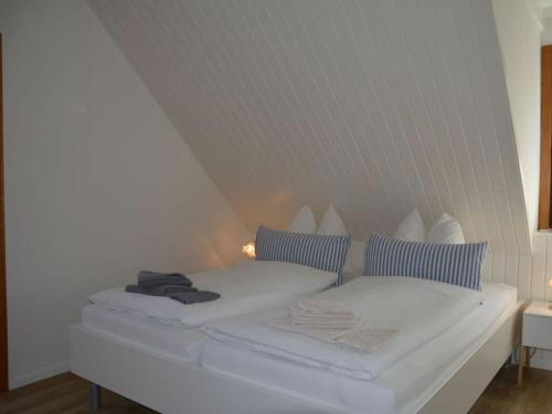 a white bed with blue pillows in a room at Langeneß Modern retreat in Steenodde