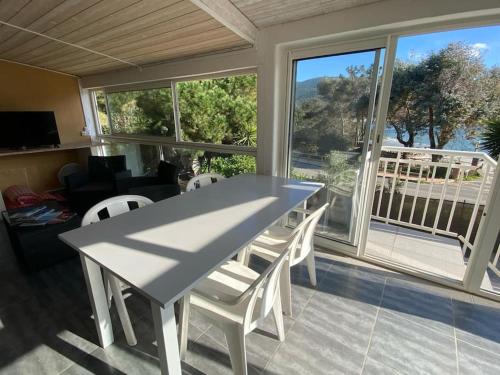 une table et des chaises blanches dans une chambre avec fenêtres dans l'établissement Appartement t3 à 50m de la plage Haut, à Pietrosella
