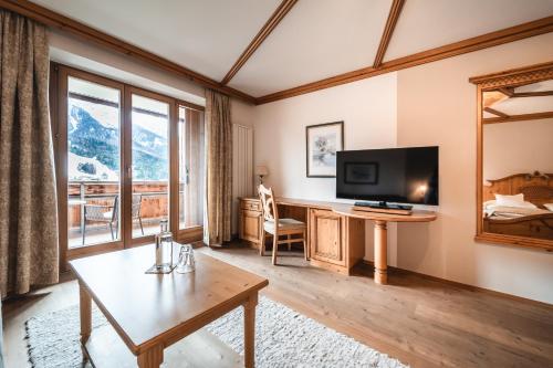 a living room with a television and a desk with a table at Naturhotel Leitlhof in San Candido