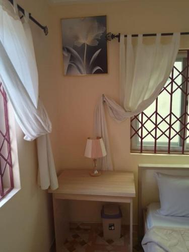 a bedroom with white curtains and a desk with a lamp at Kim's Guest House in Kasoa