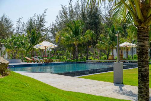 uma piscina com dois guarda-sóis e uma palmeira em KIGI Beach Resort em Phan Thiet