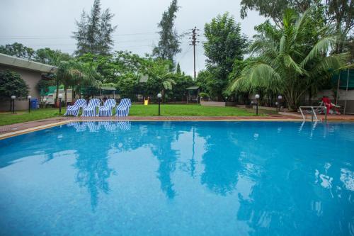 a swimming pool with blue chairs and trees at Sterling Lonavala in Lonavala