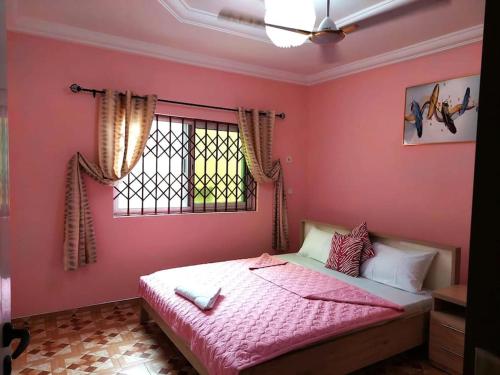 - une chambre avec des murs roses et un lit avec une fenêtre dans l'établissement Kim's Guest House, à Kasoa