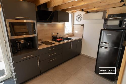 - une cuisine avec des armoires noires et un réfrigérateur noir dans l'établissement Maison rénovée et climatisée avec WIFI à 600m de la plage, à Vias