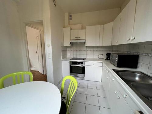 a kitchen with white cabinets and a table and yellow chairs at Appart - proche gare - 4 pers in Vaucresson