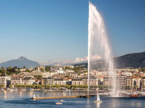 una fontana nell'acqua di fronte a una città di Fairmont Grand Hotel Geneva a Ginevra