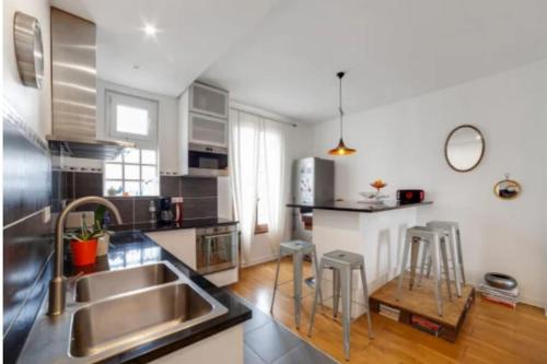 une cuisine avec un évier et un comptoir avec des tabourets dans l'établissement JO 2024 Jolie Maison avec Jardin Proche Paris, à La Garenne-Colombes