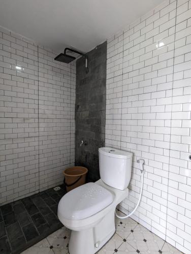 La salle de bains est pourvue de toilettes et d'un mur carrelé blanc. dans l'établissement Cottage Linggayoni Dieng 1, à Diyeng