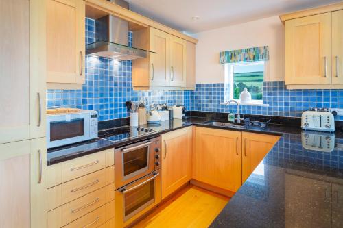 a kitchen with wooden cabinets and blue tiles at 2 Ocean's Edge in Hope-Cove