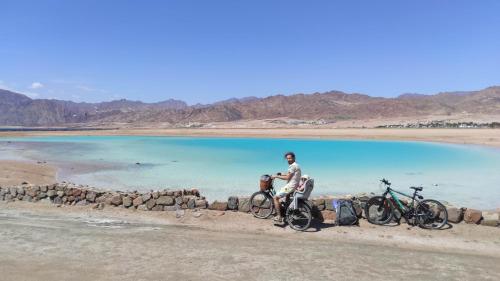 a man sitting next to two bikes in front of a body of water at Frogfish Apartment in Dahab