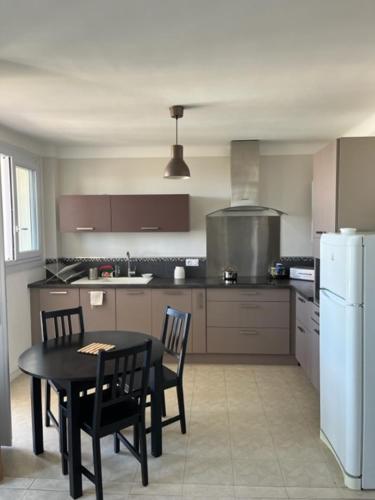 La cuisine est équipée d'une table et de chaises noires ainsi que d'un réfrigérateur. dans l'établissement T3 Corniche Sète Rare, à Sète