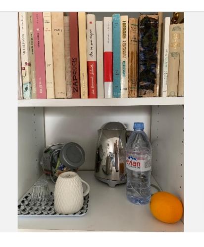 ein Regal mit Büchern, einer Flasche Wasser und einer Orange in der Unterkunft Chambres dans maison d'architecte in Suresnes