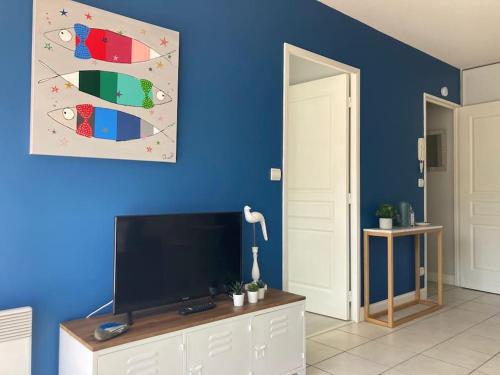 ein Wohnzimmer mit einem TV und einer blauen Wand in der Unterkunft Appartement cosy proche rue piétonne et plages in Capbreton