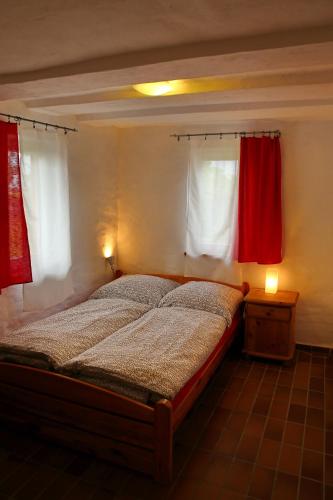 ein Schlafzimmer mit einem Bett und zwei Fenstern mit roten Vorhängen in der Unterkunft Hofboddenblick in Kückenshagen