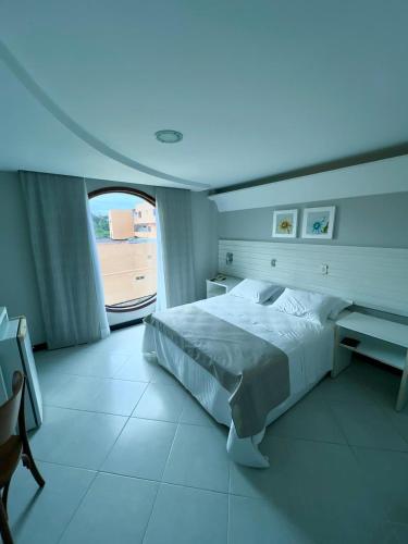 a bedroom with a bed with a desk and a window at Hotel Violeta in Guarapari