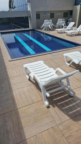 a pool with white lounge chairs next to a swimming pool at Apartamento Flat Palladium completo e mobiliado in São Vicente
