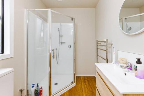 La salle de bains blanche est pourvue d'une douche et d'un lavabo. dans l'établissement Tranquil Countryside Retreat with Modern Amenities, à Pokeno