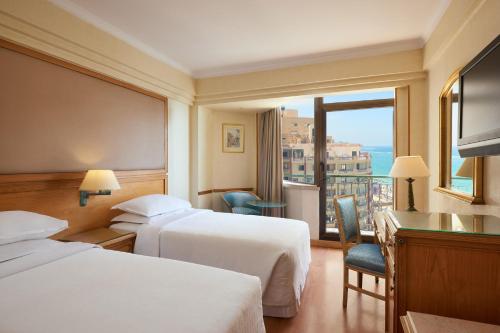 アレクサンドリアにあるシェラトン モンタザ ホテルのベッド2台とバルコニーが備わるホテルルームです。