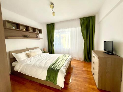 1 dormitorio con 1 cama con cortinas verdes y TV en Valcea Northside Spacious Apartment en Râmnicu Vâlcea