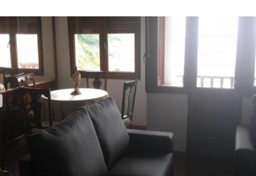 a living room with a couch and a table with windows at Piso con vistas al puerto in Lastres