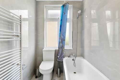 a bathroom with a toilet and a tub and a window at Beautiful Wembley Gem - Parking -Sleeps 14 in London