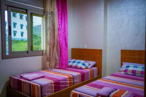2 Betten in einem Zimmer mit rosa Vorhängen in der Unterkunft شقق العمري أقشور شفشاون in Akchour